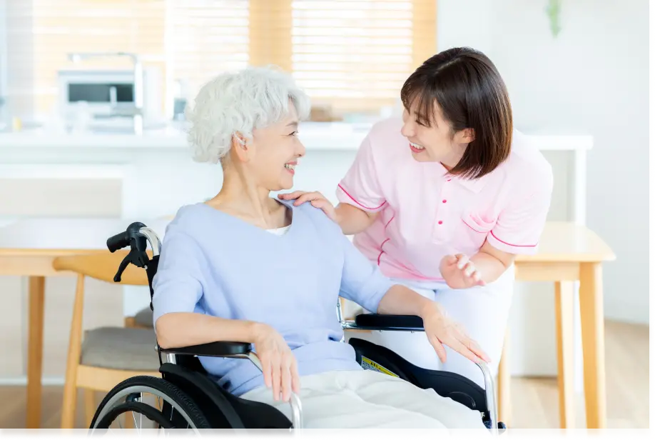 車椅子の高齢女性とスタッフが自宅で笑顔で会話している在宅医療の様子