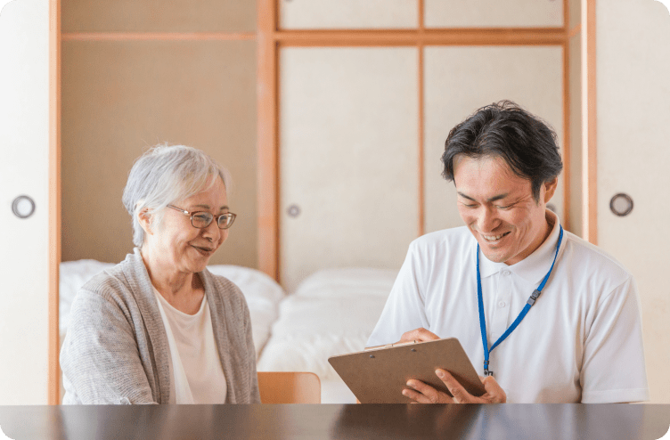 高齢女性と男性医療従事者が自宅でカルテを見ながら相談している様子
