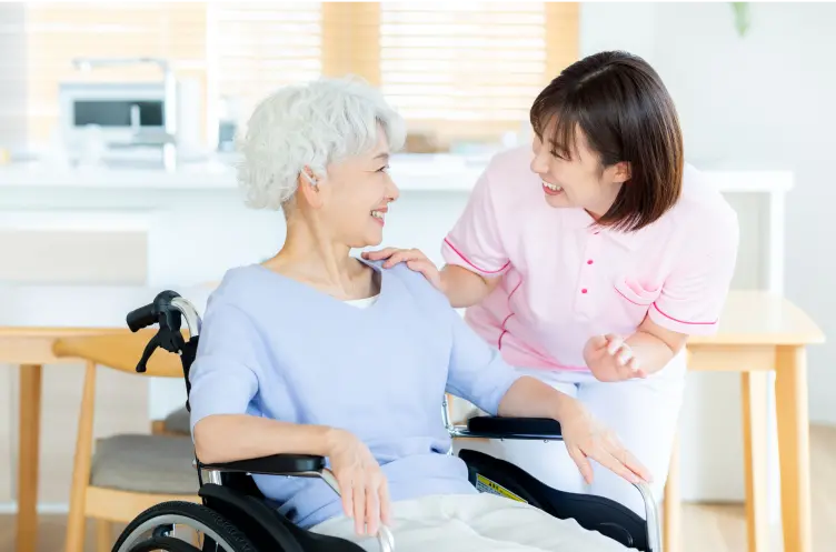 車椅子の高齢女性と医療従事者が自宅で笑顔で会話している様子